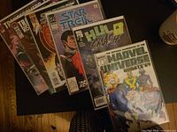 Fanned stack of seven bagged comic books showing visible titles and protective sleeves