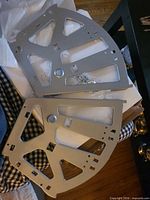 Two silver quarter-circle hinge brackets with screws in bag