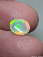 Front view of oval opal on fingertip showing play-of-colour