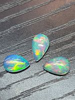 Three pear cabochon opals showing play of colour on black textured background