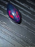 Top view of marquise opal on textured surface showing red and blue flash