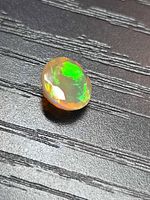 Round faceted opal showing bright green flash on dark background