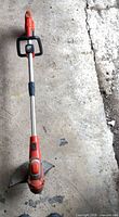Full length view of orange 24V cordless string trimmer on concrete floor