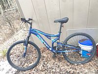 Full view of blue Hyper Bear Mountain 26-inch mountain bike leaning against shed
