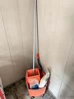 Full view of orange mop bucket with wringer, mop handle, packaged refill