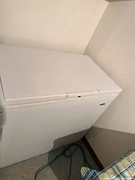 Closed white chest freezer in corner with power cord visible