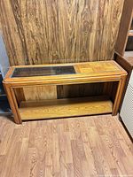Front view of honey oak console table showing glass panel, parquet inlay, lower shelf