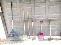 All five long-handled tools lined up against garage door