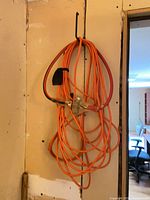 Coiled orange extension cord with metal three-way splitter hanging on wall