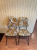 Front view of both chairs showing floral vinyl upholstery and metal legs