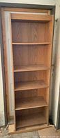 Full frontal view of tall oak-finish bookcase showing five fixed shelves