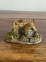 Front view of resin cottage figurine showing door, thatched roof and picket fence