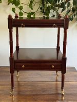Front view of dark wood Bombay Company side table showing top surface, middle shelf, lower drawer and brass casters