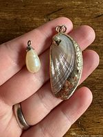 Hand holding shell pendant and faux pearl pendant for scale