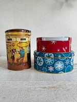 Group shot of three cylindrical tins: Tim Hortons tin left, blue and red snowflake tins stacked right