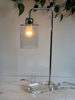 Full view of lit chrome table lamp with clear bubble shade on acrylic base