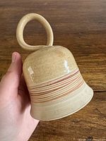 Angled view of ceramic bell showing cream glaze and stripe band