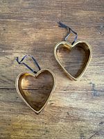 Two hollow gold-tone ceramic heart ornaments with ribbons on wooden surface