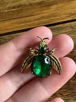 Front view of gold-tone bee brooch with green rhinestone body