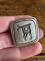 Front view of square metal brooch showing stylized animal design
