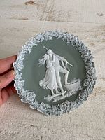 Front view of round bisque wall plate showing couple relief and floral border