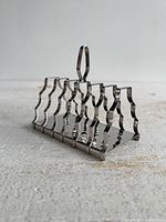 Perspective view of stainless steel toast rack showing wavy divider bars and loop handle