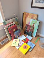 Group of stacked and floor-laid canvases of varied subjects and sizes