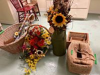 Group view of four wicker baskets, green metal jug with sunflowers, decorated broom, mixed floral arrangement