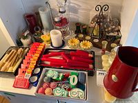 overview of assorted candles, candleholders, red pitcher and accessories on shelf