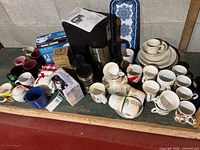 Overview showing coffeemaker, serving tray, tumblers, boxed items, mugs, dinnerware