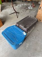 Blue plastic tote with lid next to gray tote with brown lid