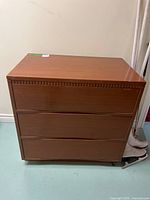 Front view of brown veneer dresser showing three drawers and decorative top trim