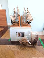 Pair of wooden ship bookends atop box; plastic-wrapped ship model on floor