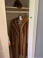Coat hanging in closet with matching hat on shelf