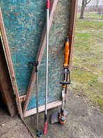 Three long-handle garden tools leaning against shed wall
