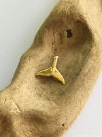 Front view of yellow gold whale tail pendant on driftwood
