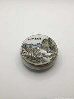 Top view showing hand painted landscape on lid of round porcelain paste box