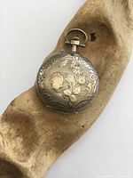 closed pocket watch showing engraved floral silver case