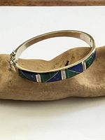 Sterling silver hinged bangle showing malachite and lapis inlay pattern and safety chain
