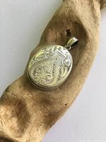 Front view of engraved silver locket on wood prop