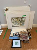 Stack of matted watercolours, books, frames and loose supplies on floor