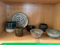 Shelf view showing decorative plate, bowls, cups, vessel