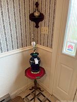 Full view of lamp on pedestal table beneath wall shelf and vase