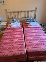 Front view of brass headboard, twin mattresses, bedding stacks