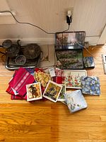 Entire lot laid out showing textiles, placemats, metal tray, teapot, perforated plate, postcards and glass dish