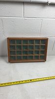 Full view of wood-framed glass-front display shelf with measuring tape for scale