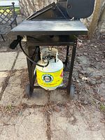 Full view of grill on cart with side shelf, wheels and propane tank attached