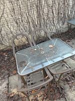 Table and two chairs showing glass top, metal frames, debris and wear