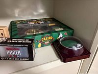 All four items on shelf: boxed roulette set, boxed chip reloader, dice shaker, wooden score box