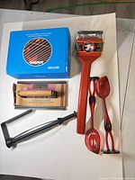All items grouped: boxed griddle kit, grill press, red grill brush, tongs, red spoons